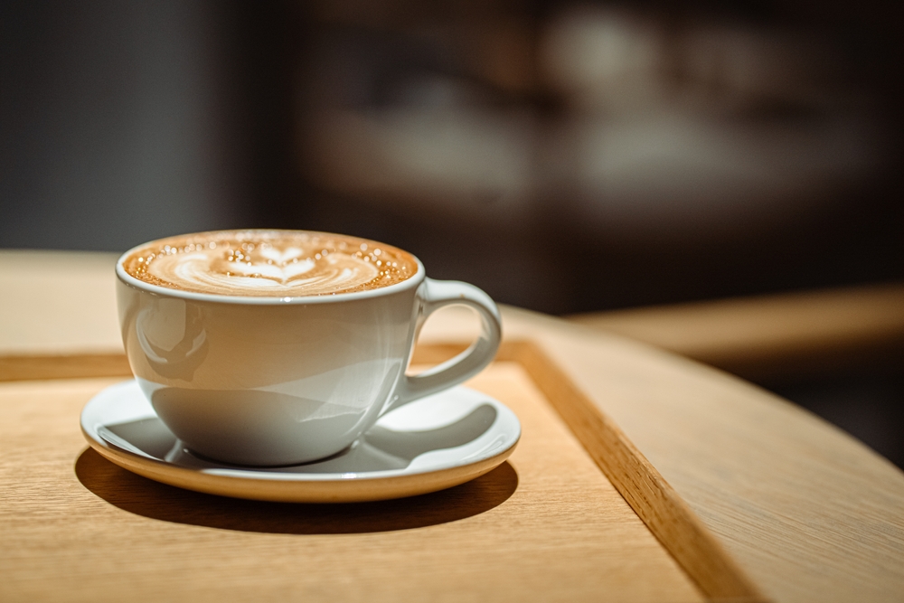 Side view of hot latte coffee with latte art in a white cup on wooden table