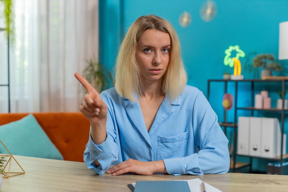 Portrait of Caucasian young business woman shakes finger, saying No be careful scolding and giving advice to avoid danger mistake disapproval sign at office. Confident freelancer girl at desk at home.