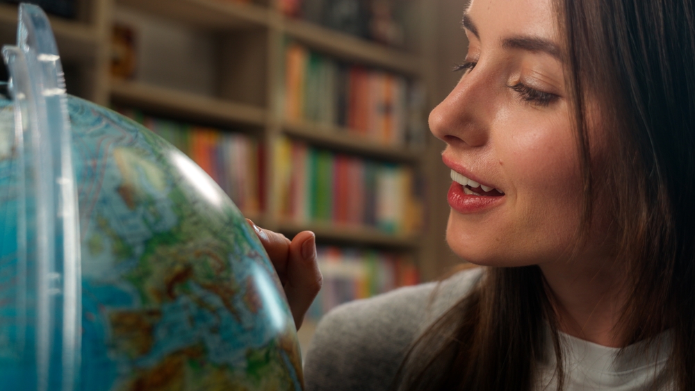 Excited Caucasian woman female girl student teacher library school geography lesson model planet earth spinning dreaming choose country vacation globe pointing finger campus learner college university