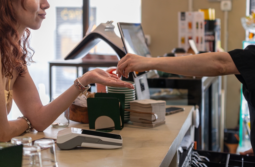 Barista handing change to female customer at coffee shop counter. Unrecognizable people