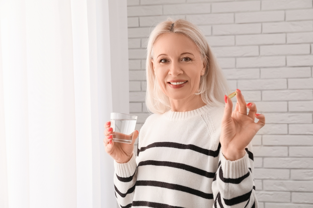 Mature woman with fish oil pills near white brick wall