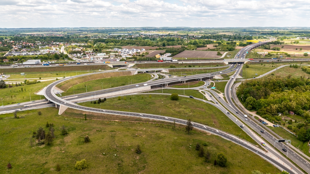 Aerial view of a large highway interchange in Poland with overpasses and surrounding fields showing complex road infrastructure and traffic planning