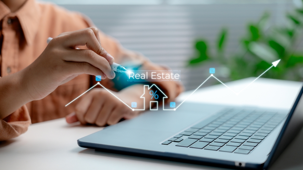 Hand analyzing real estate investment trends with digital interface on laptop, showing housing market growth, property value, interest rates, and smart investment technology.