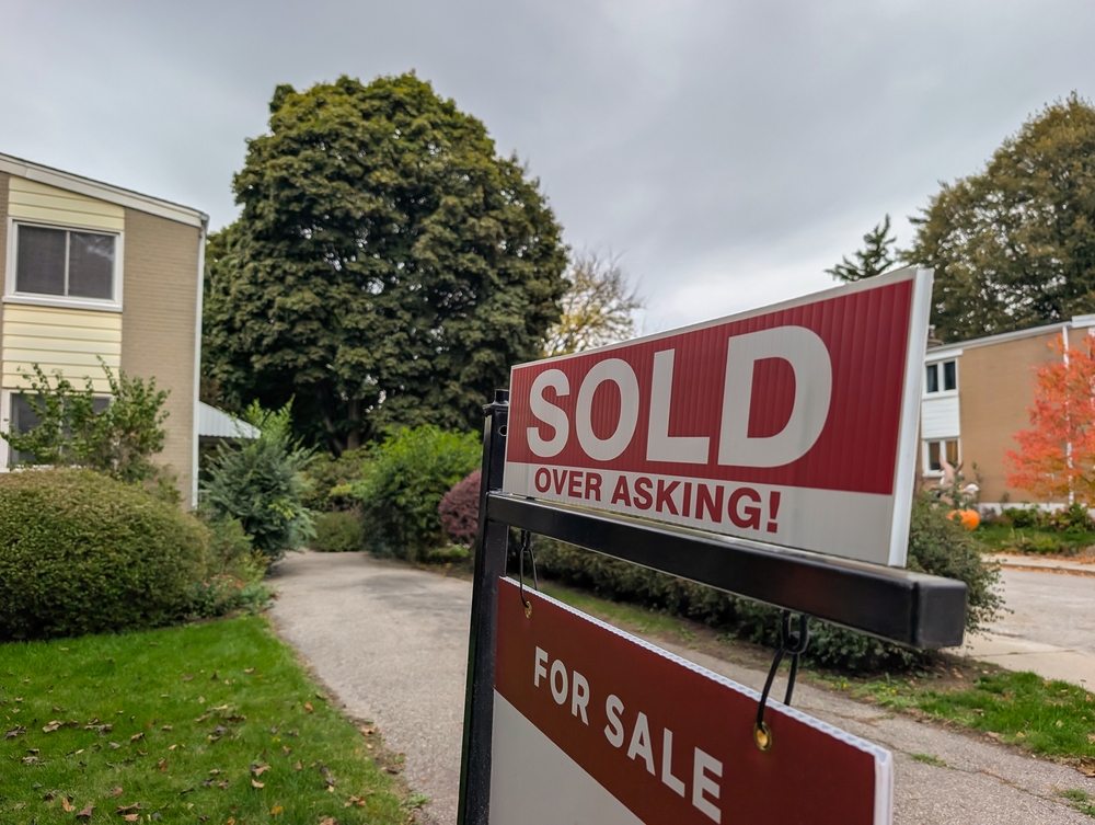New sign sold over asking price for sale in front of detached house in residential area. Real estate bubble, crash, hot housing market, overpriced property, buyer activity concept. Selective focus.