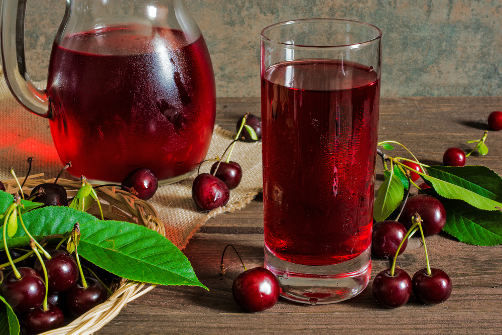 cold cherry juice in a glass and pitcher on wooden table with ripe berries in wicker basket