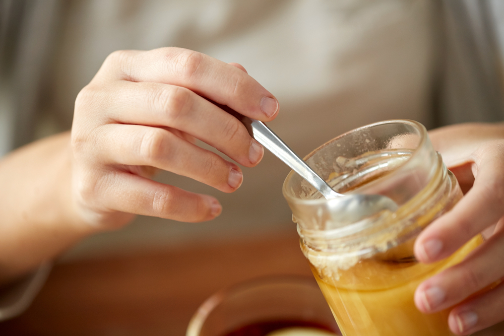 health, traditional medicine and ethnoscience concept - close up of woman hands with honey jar and spoon