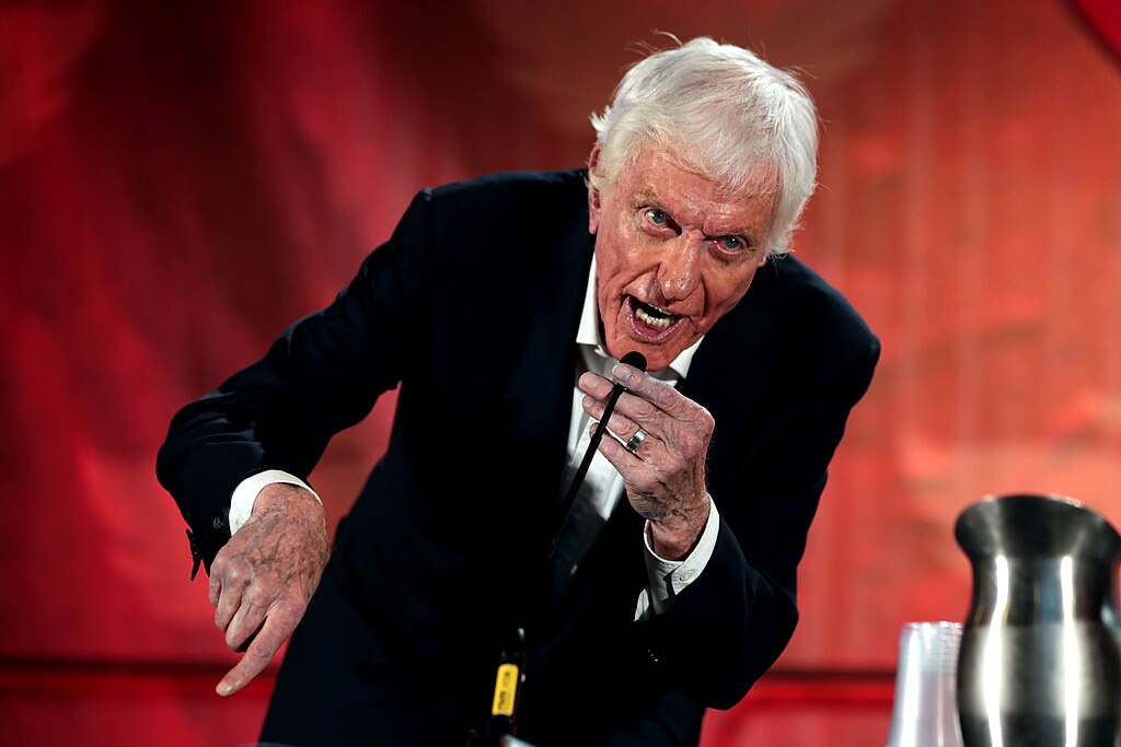 Dick Van Dyke leaning forward and speaking animatedly into a microphone at the same panel event.