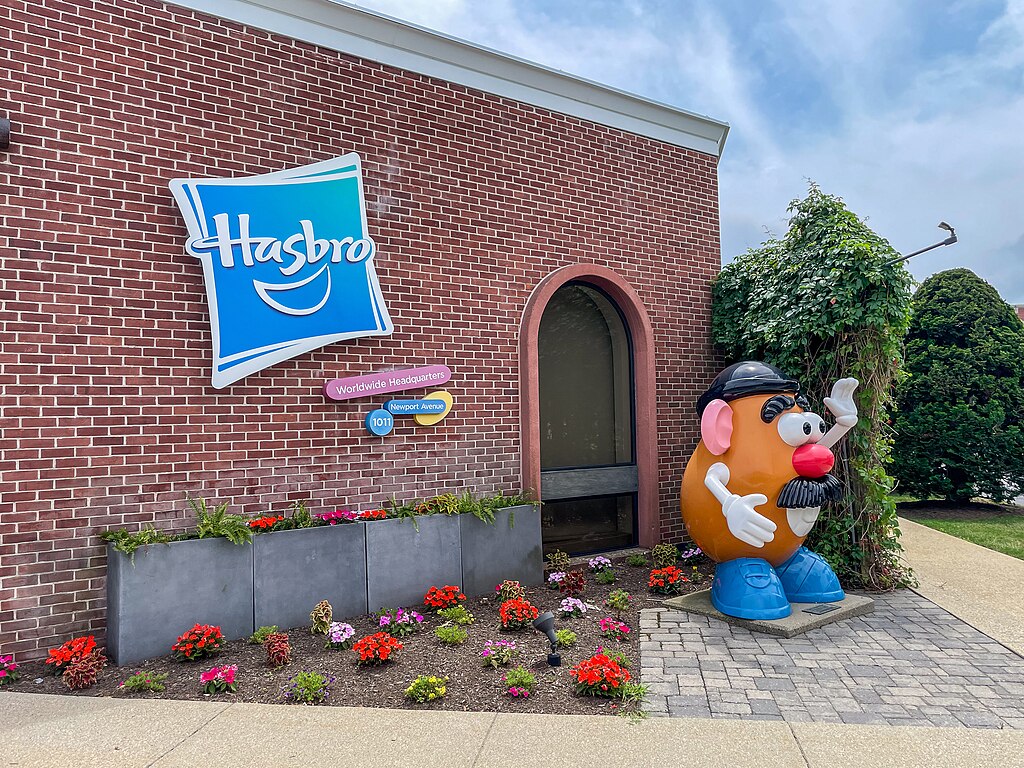 Brick Hasbro building with the blue logo and a large Mr. Potato Head statue out front surrounded by flowers.
