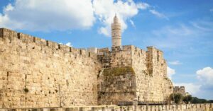 Ancient Assyrian Inscription Found in Jerusalem May Reveal Truth Behind Biblical Story An ancient stone fortress with high walls and a tall tower rises against a bright blue sky with scattered clouds.