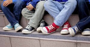 A row of children sitting on outdoor steps, showing only their legs and colorful sneakers