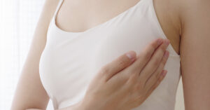 Woman wearing white tank top, cupping her breast. Breast cancer lump self examination concept