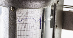 Close-up of a meteorological chart recorder, showing a blue line tracing a measurement over time.