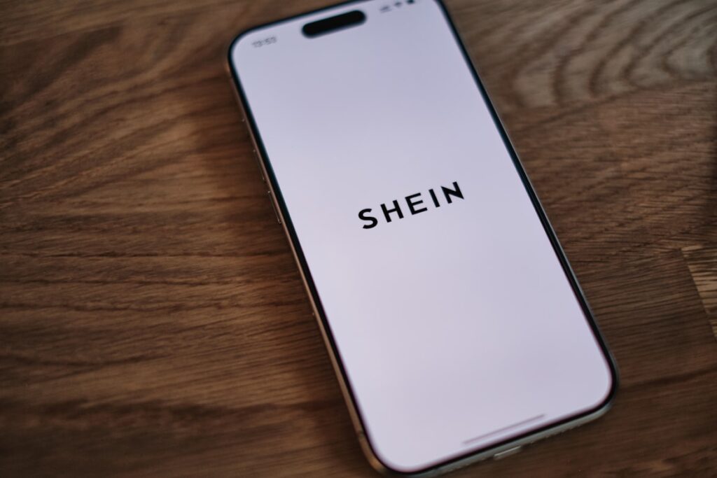 iPhone on a wooden table displaying the Shein app loading screen.