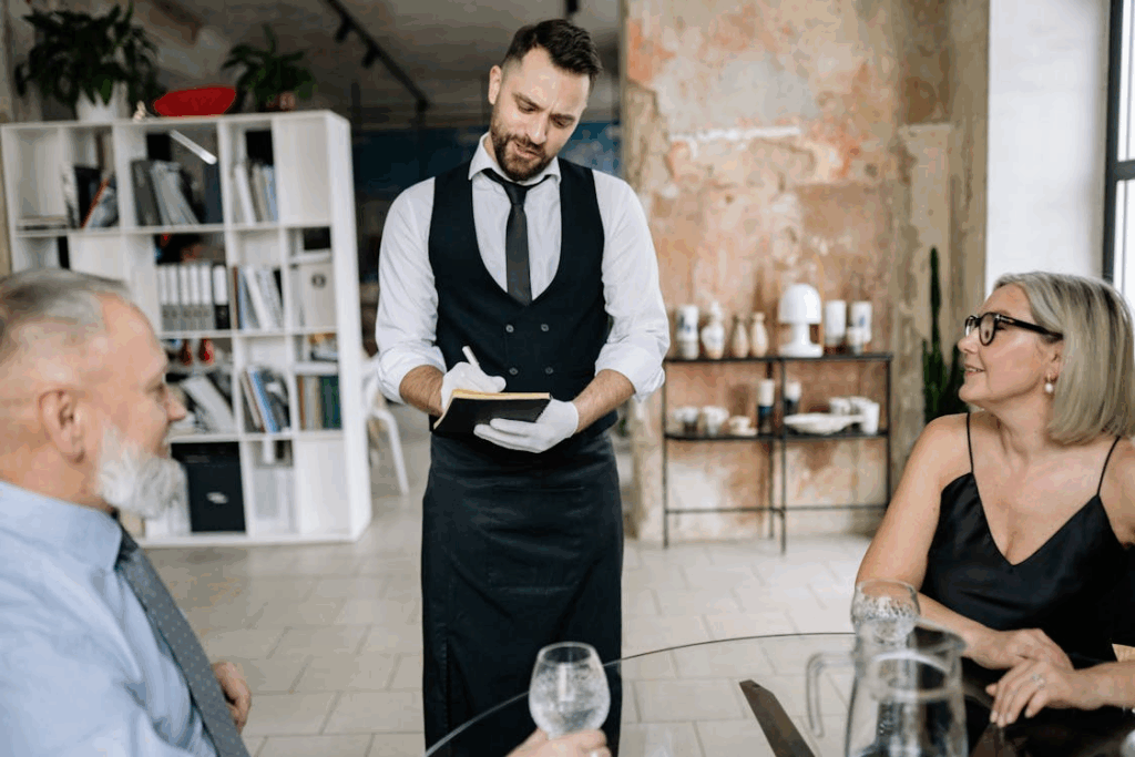 Waiter Taking Order from Customers at a Glass Table in an Elegant Interior with Textured Walls