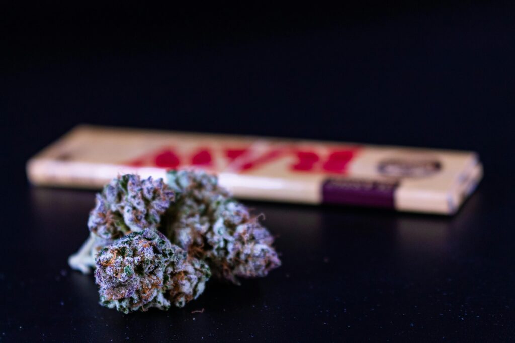 A cannabis bud in sharp focus with a package of RAW rolling papers blurred in the background.