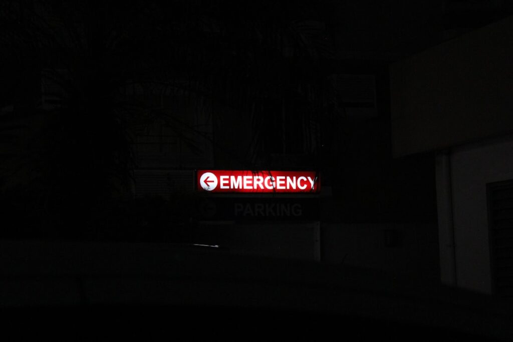 A red illuminated "Emergency" sign glows against a dark nighttime background.