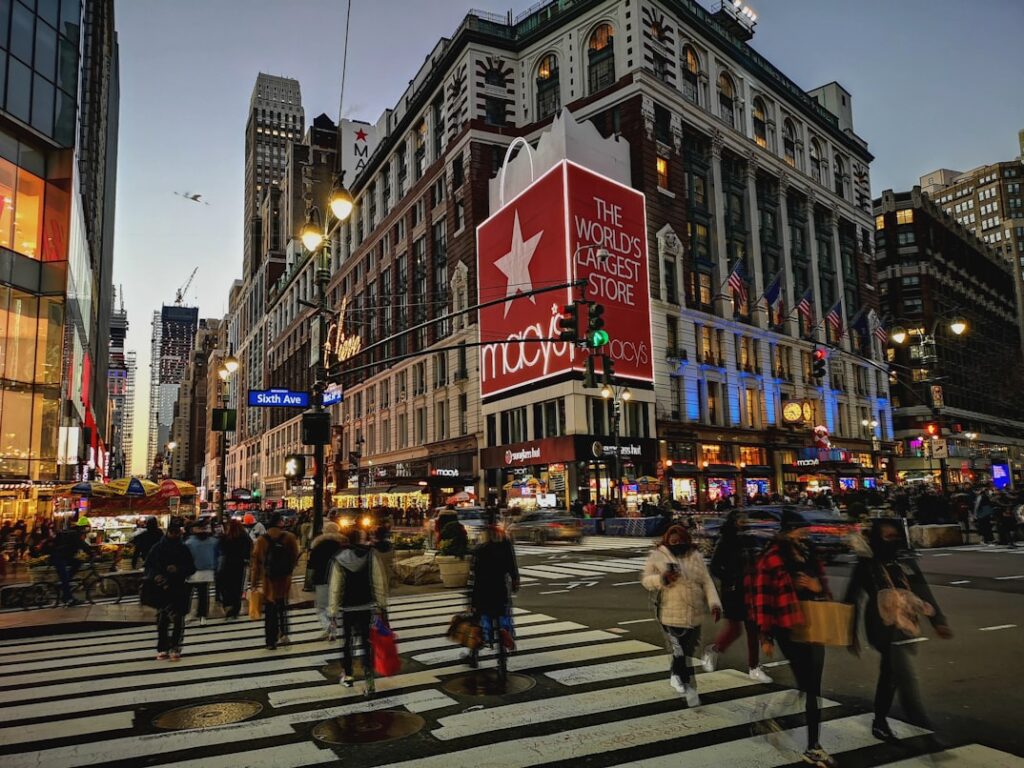 Macy's flagship store in Herald Square at dusk, pedestrians crossing the street in front of the building with its red star logo.