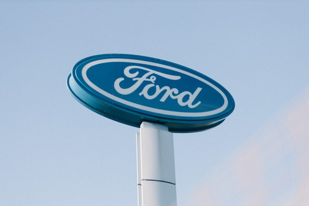 Ford dealership sign on a tall pole showing the blue oval logo against a pale sky.