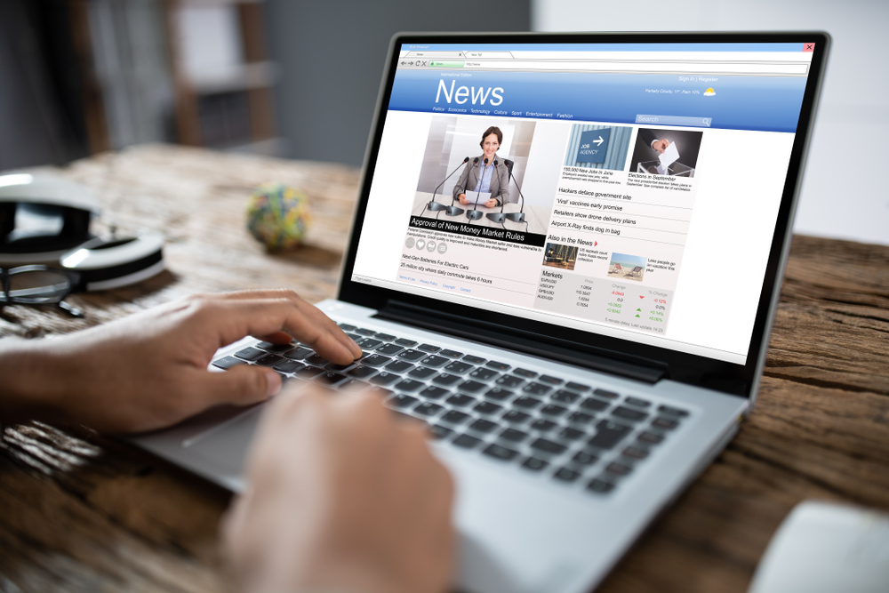 Close-up Of Businessperson Checking Online News On Laptop At Desk