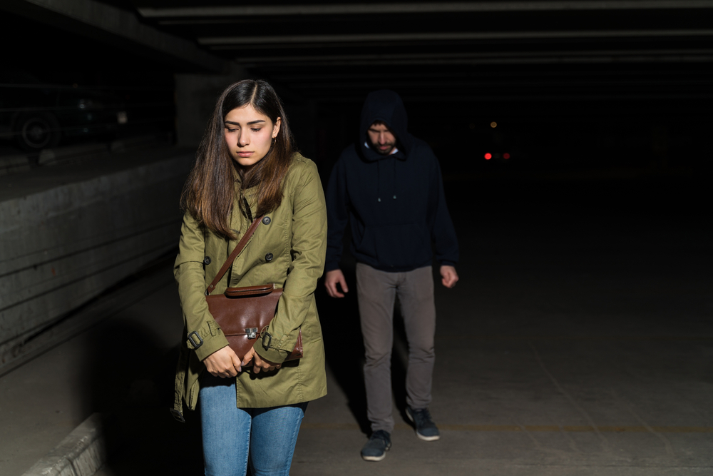Frightened Latin woman being followed by robber in dark parking lot