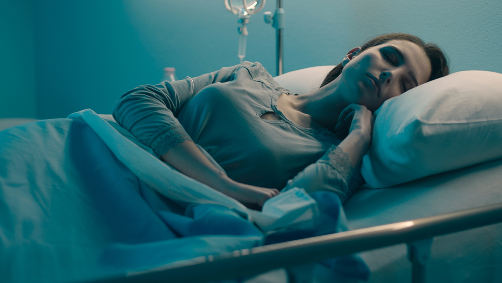 Young woman lying in a hospital bed at night and sleeping with IV drip