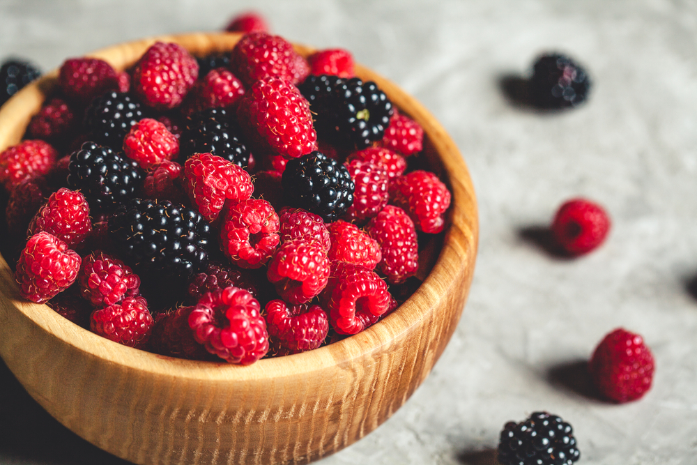 raspberries and blackberries in wood bowl on gray table, vintage