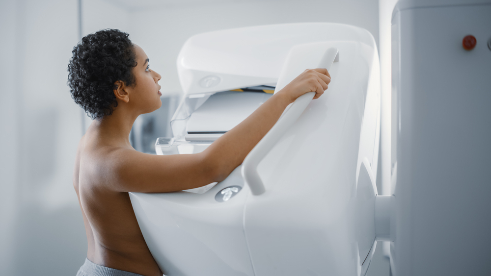 In the Hospital, Portrait Shot of Topless Latin Female Patient with Short Hair Undergoing Mammography Screening Procedure. Healthy Young Female Does Cancer Preventive Mammogram Scan in Radiology Room.