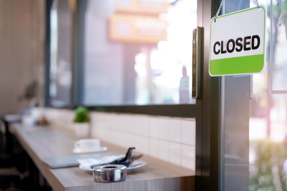 Open and closed flip sign in front of coffee shop and restaurant glass door. Wooden sign with wording of place's status CLOSED