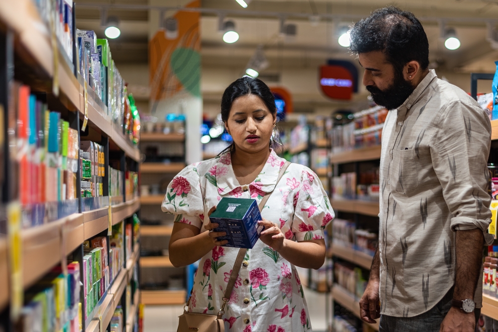 An urban Indian couple read and discuss the contents of a box of sweets while standing in the middle of retail store aisle in New Delhi.