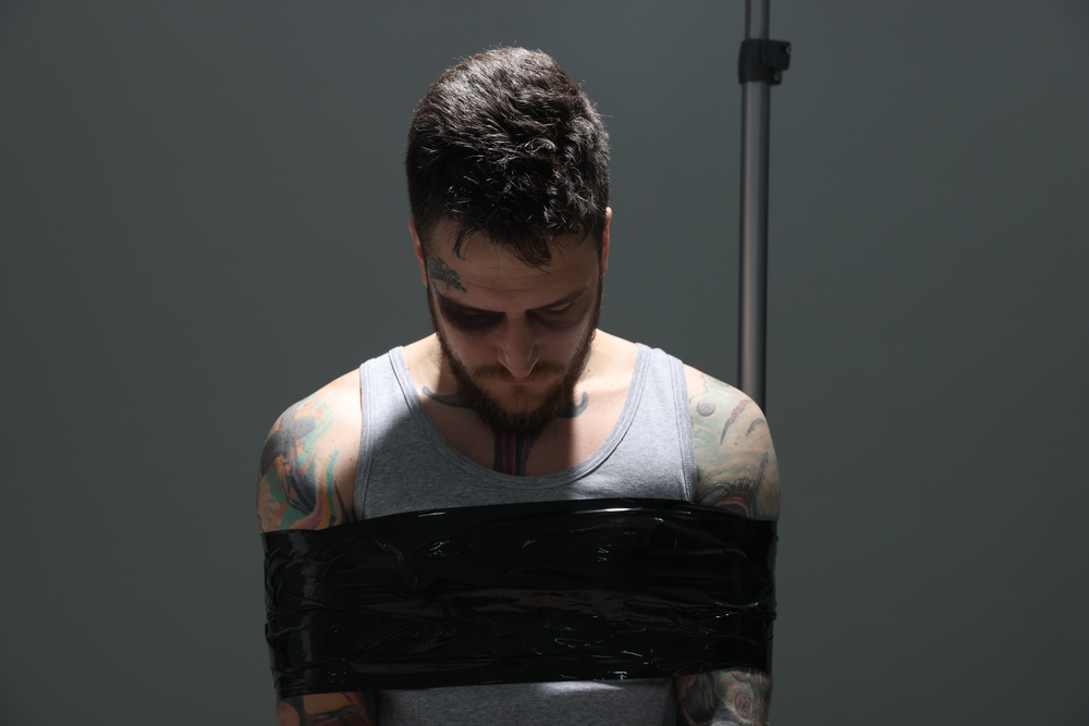 Man with bruise taped up and taken hostage on grey background