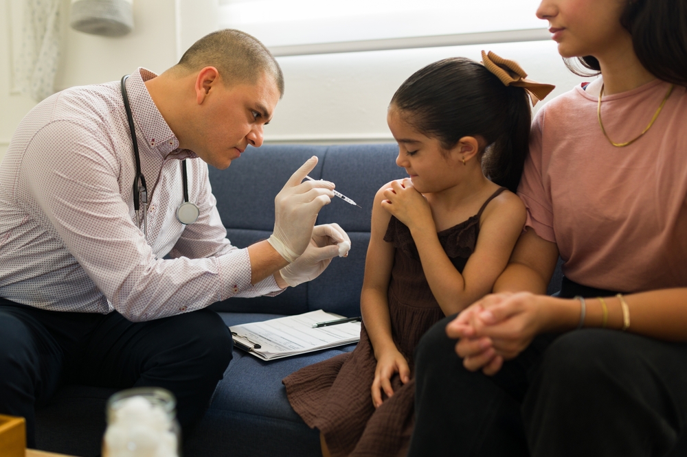 Sick latin kid having a doctor's visit getting an medicine injection or vaccine from a pediatrician in the company of her mom