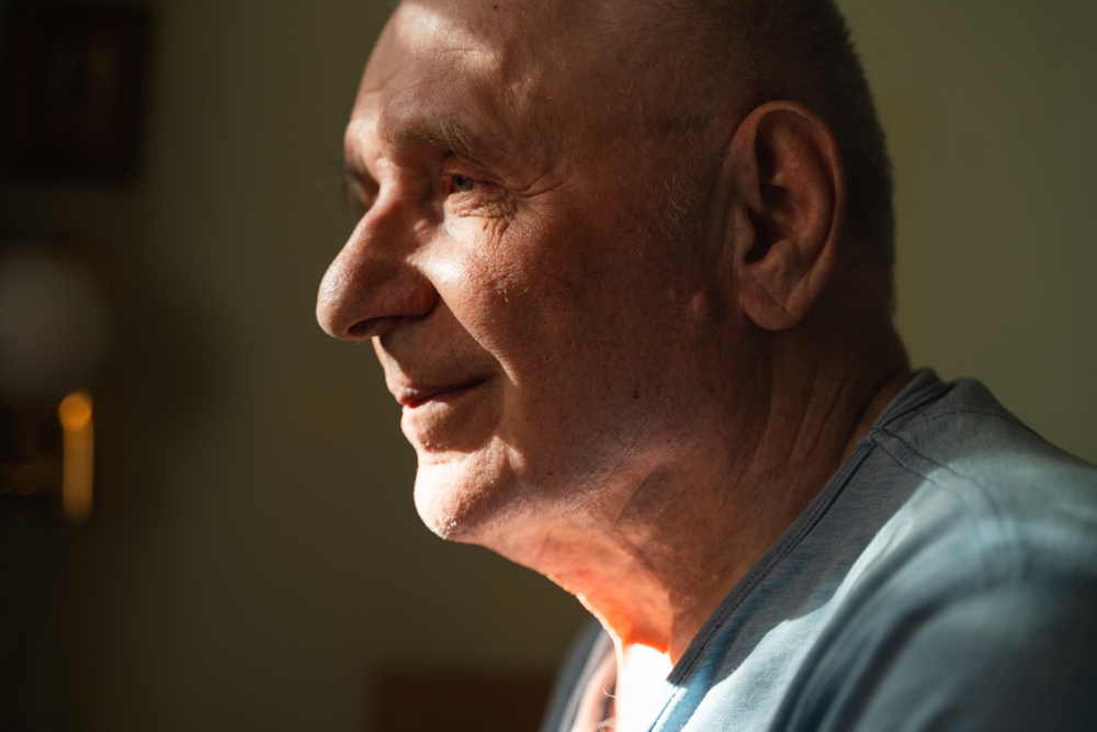 Elderly senior man at home in shadow and sunlight with headache. Retirement medical problems, high blood pressure. 