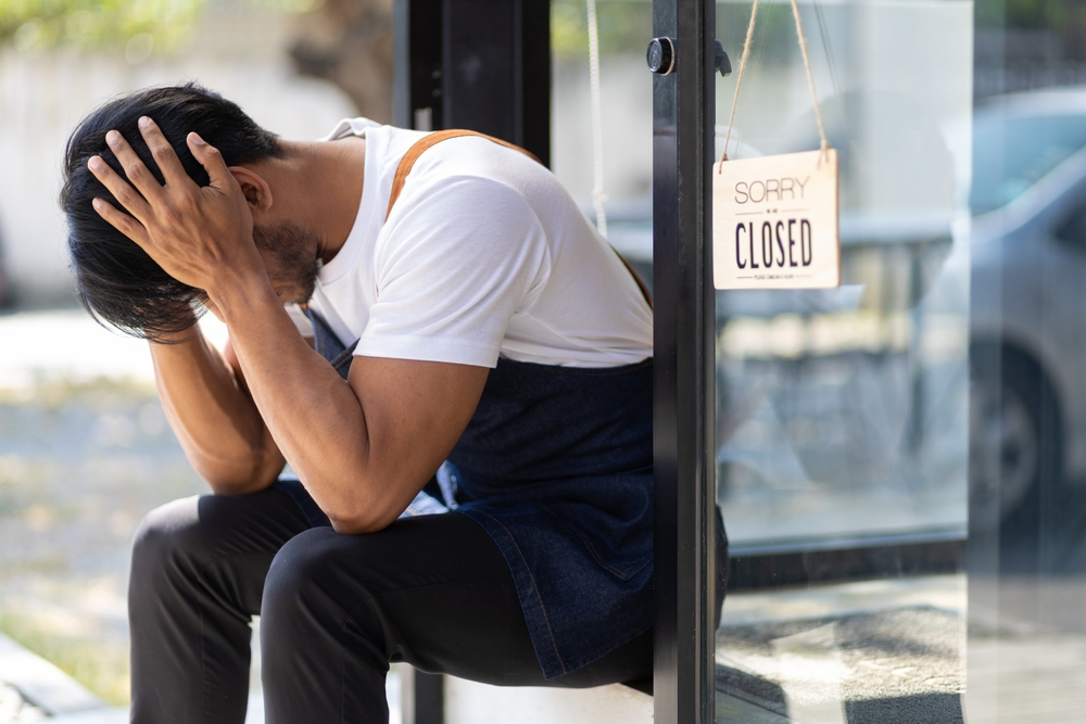 Young man running a small start-up business sits at the entrance looking absent-minded. Entrepreneurs starting small startups are stressed out and forced to close shop due to the economic crisis.