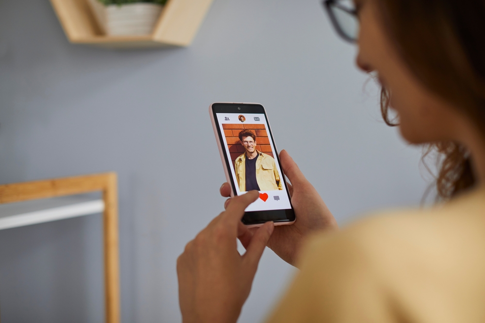 Young woman using dating app on mobile phone. Woman pressing red heart like button at handsome man profile photo while using relationship site or application. Find love online concept