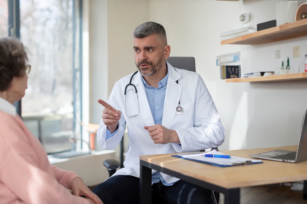 Middle aged male doctor consulting senior female patient in clinic, GP have consultation with elderly woman client in private hospital