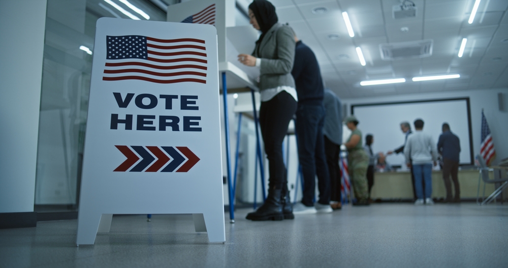Vote here sign on the floor. Multi ethnic American citizens vote in booths in polling station office. National Election Day in United States. Political races of US presidential candidates. Civic duty.