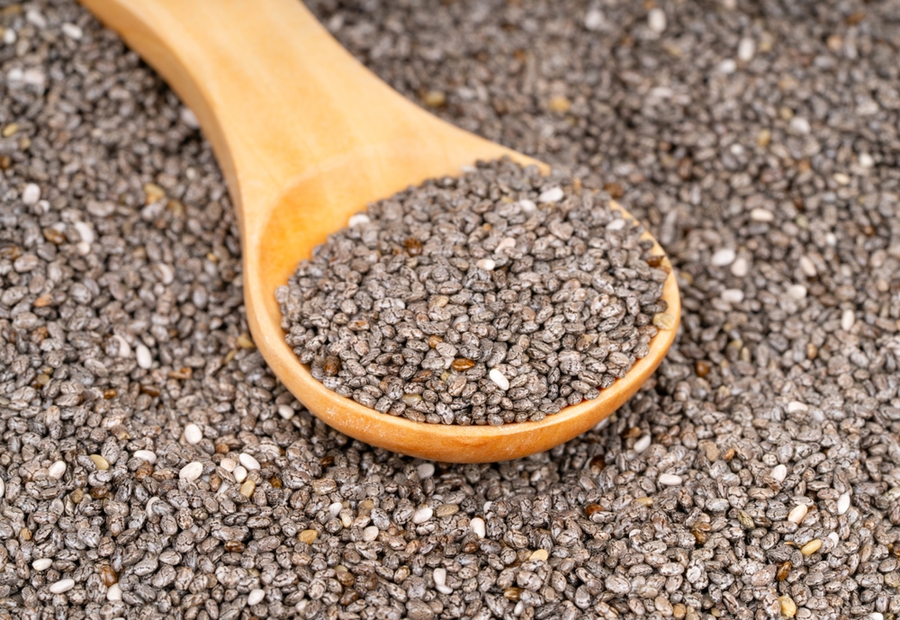 Scattered chia seeds with wooden spoon close up
