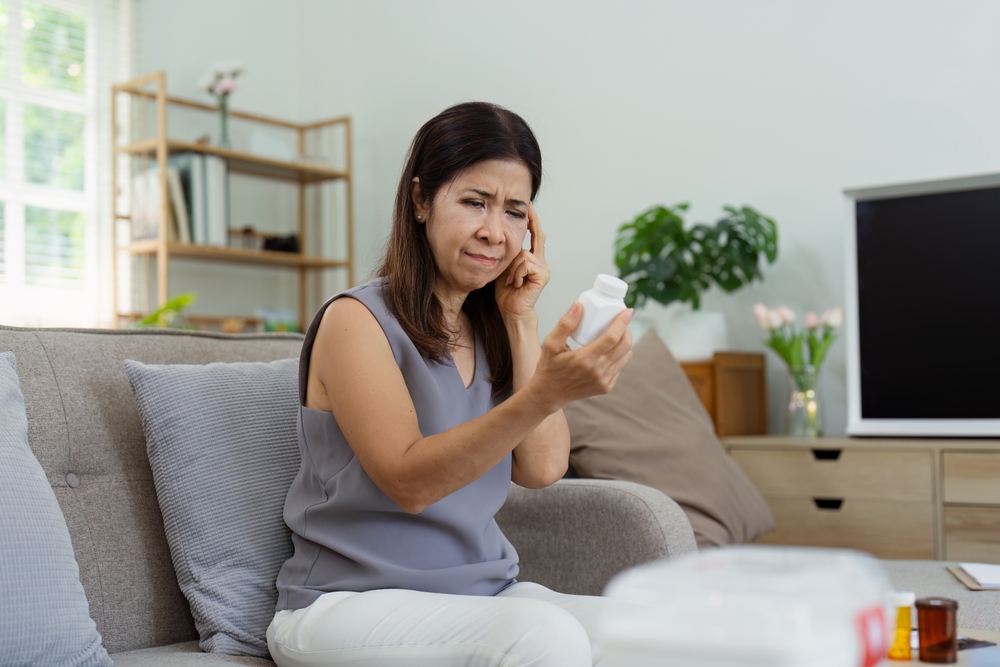 Middle-aged Woman Reading Medication Bottle Label While Sitting on Couch in Modern Living Room with Natural Light and Cozy Decor