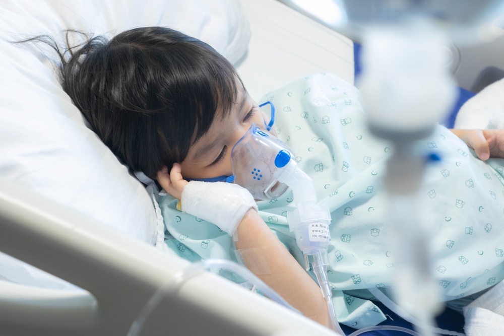 an Asian toddler boy has Cold or Flu or influenza or asthma or pneumonia disease and need nebulizations,Sick boy rest on patient bed in hospital and has inhalation therapy by the mask of inhaler.Sick 