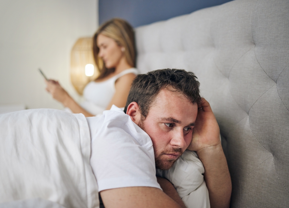 Phone, thinking and man in bed with cheating wife, infidelity or affair in online chat at home with stress. Marriage conflict, divorce or couple on mobile app with betrayal or upset husband in house