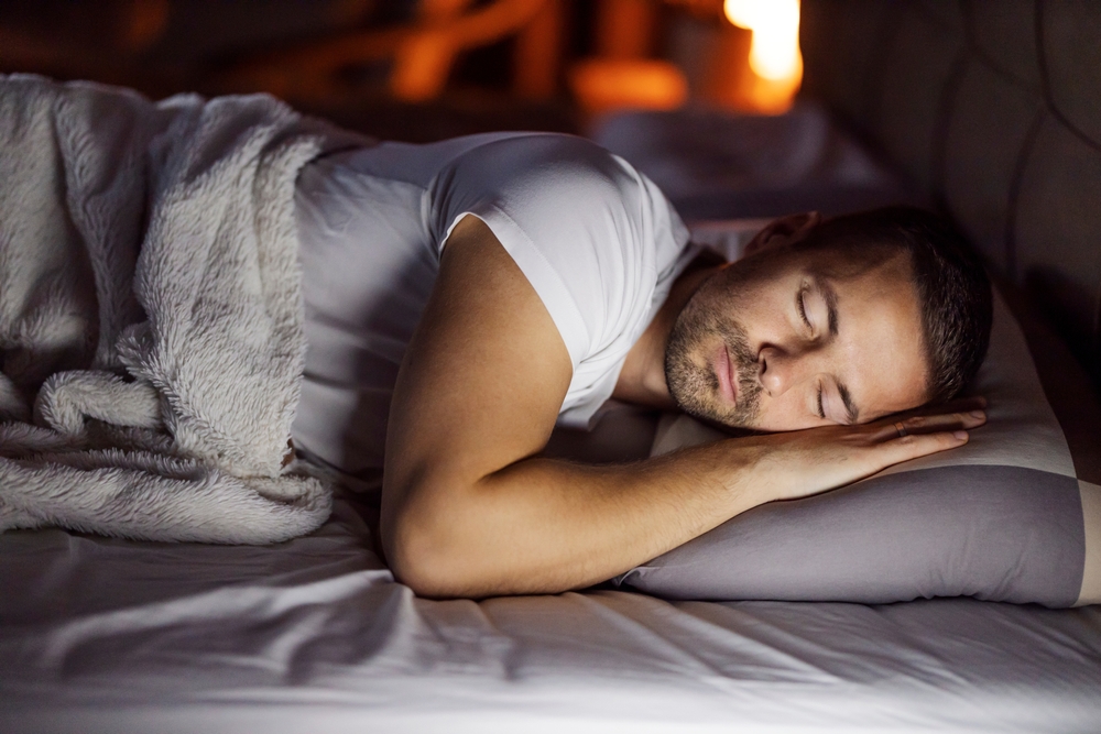 Young tired man is sleeping deeply on a pillow in dark bedroom at night.