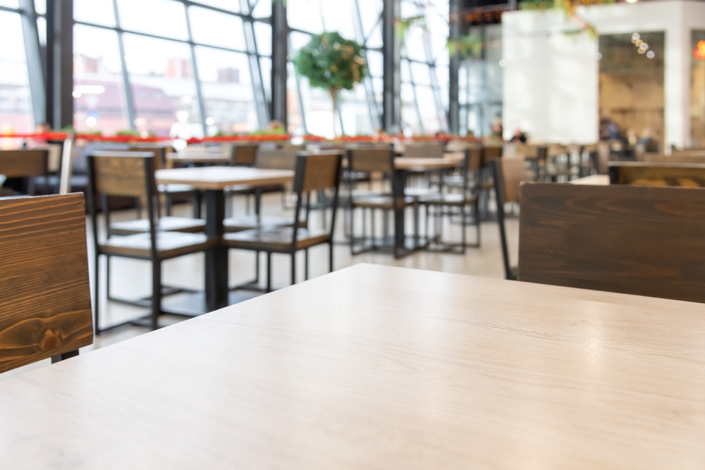 Close-up view of empty wooden tables of food court in shopping mall. Focus on table surface. Copy space for your text or decoration. Restaurant and cafe furniture. Food business theme.