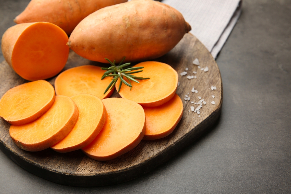 Fresh raw sweet potatoes, rosemary and salt on gray table, closeup