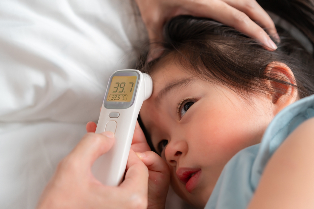 A caring parent checks the temperature of a young child using a digital thermometer at home, highlighting concern and the importance of monitoring health during illness.
