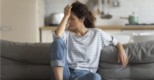 Millions Suffer Extreme Fatigue from a Condition Most People Don’t Recognize Exhausted frustrated young woman touching forehead, sitting on couch alone, suffering from strong headache or migraine, worried girl thinking about problems, divorce or break up, lost in thoughts