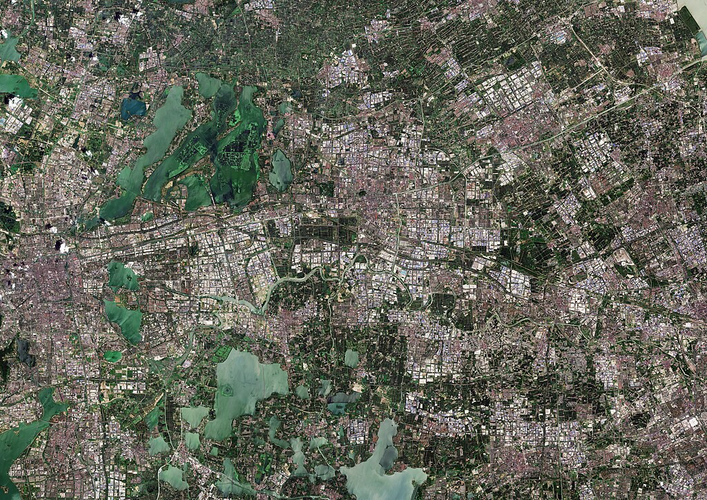 Satellite view of a sprawling metropolitan area showing dense urban development interspersed with green spaces and waterways.