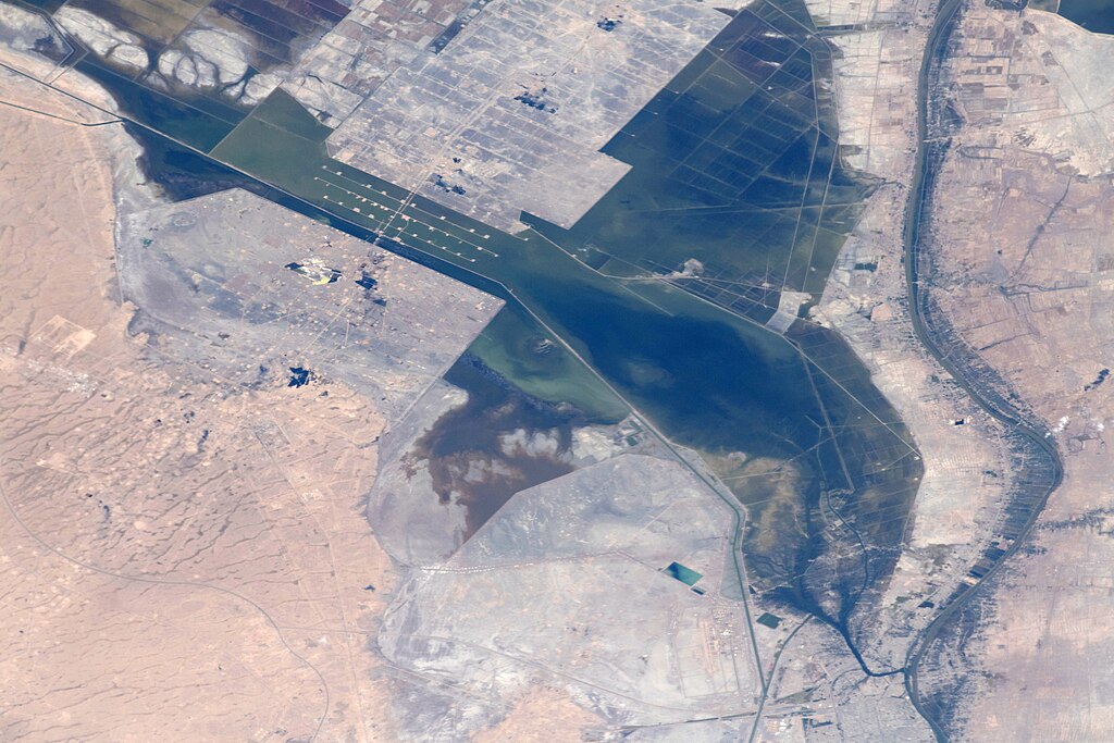 Aerial view of geometric blue-green wetland pools in an otherwise arid desert Iraq landscape, showing managed water systems fed by a river channel