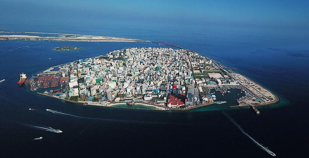 Aerial view of Malé, the densely built capital of the Maldives, showing the entire island packed with buildings and surrounded by open ocean just meters from its edges.