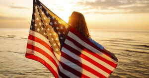 Woman holding an American Flag behind her while on beach at sunset