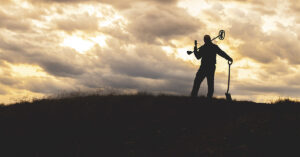 Metal Detector Hobbyist Unearths Ancient Celtic Gold Coin silhouette of a person using a metal detector during sunset.